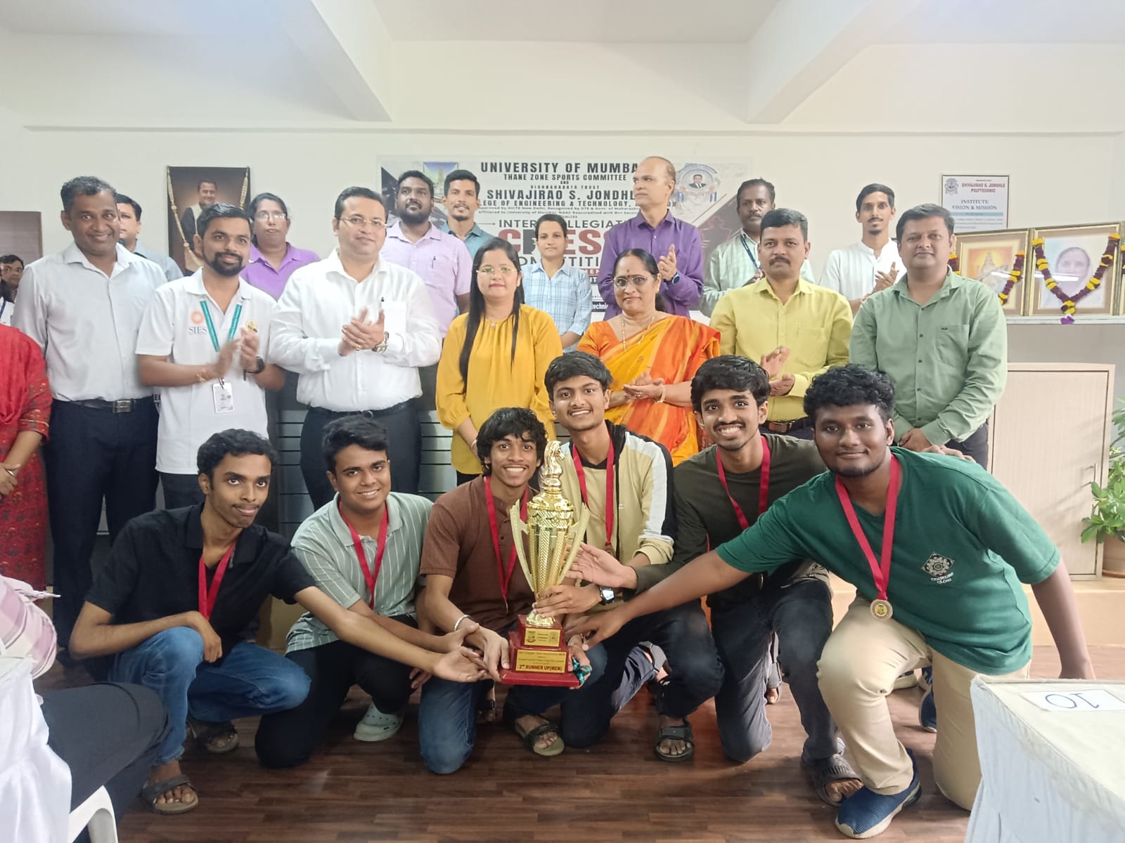 Students with faculty at a University of Mumbai intercollegiate event, holding a trophy